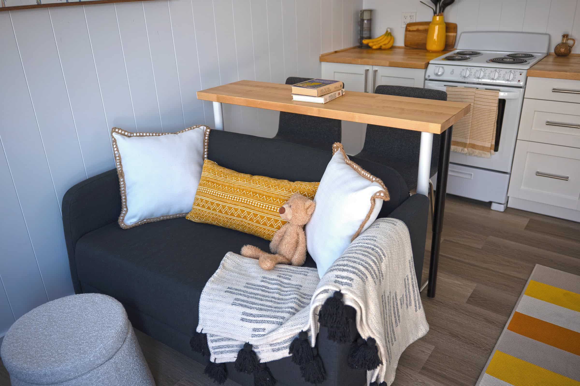Jason living and kitchen: white shaker cabinets, butcher-block veneer, grey sofa, white slide-in range, light vinyl floor, white paneling
