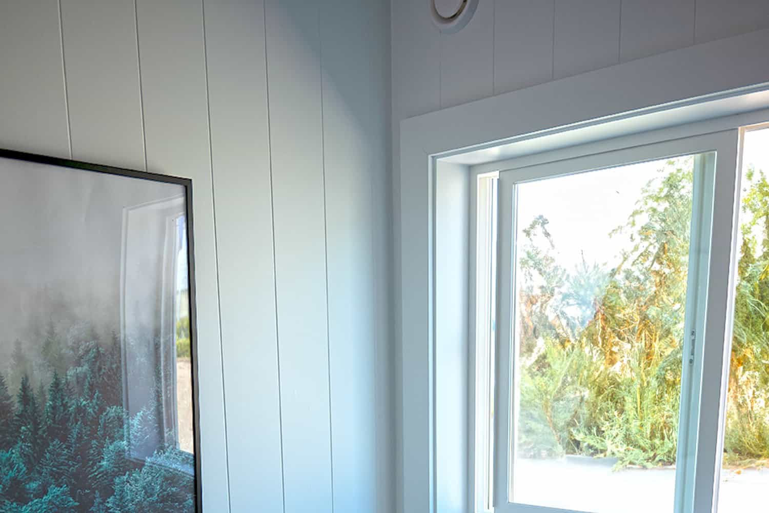 Window corner of the Jason ADU: pale vertical paneling, white-framed window, forest print on the adjacent wall