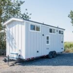Mint STR 26 tiny house on a dual-axle bumper-pull trailer: light grey vertical siding, white trim, dark standing-seam roof, high loft windows, white mini-split on the tongue