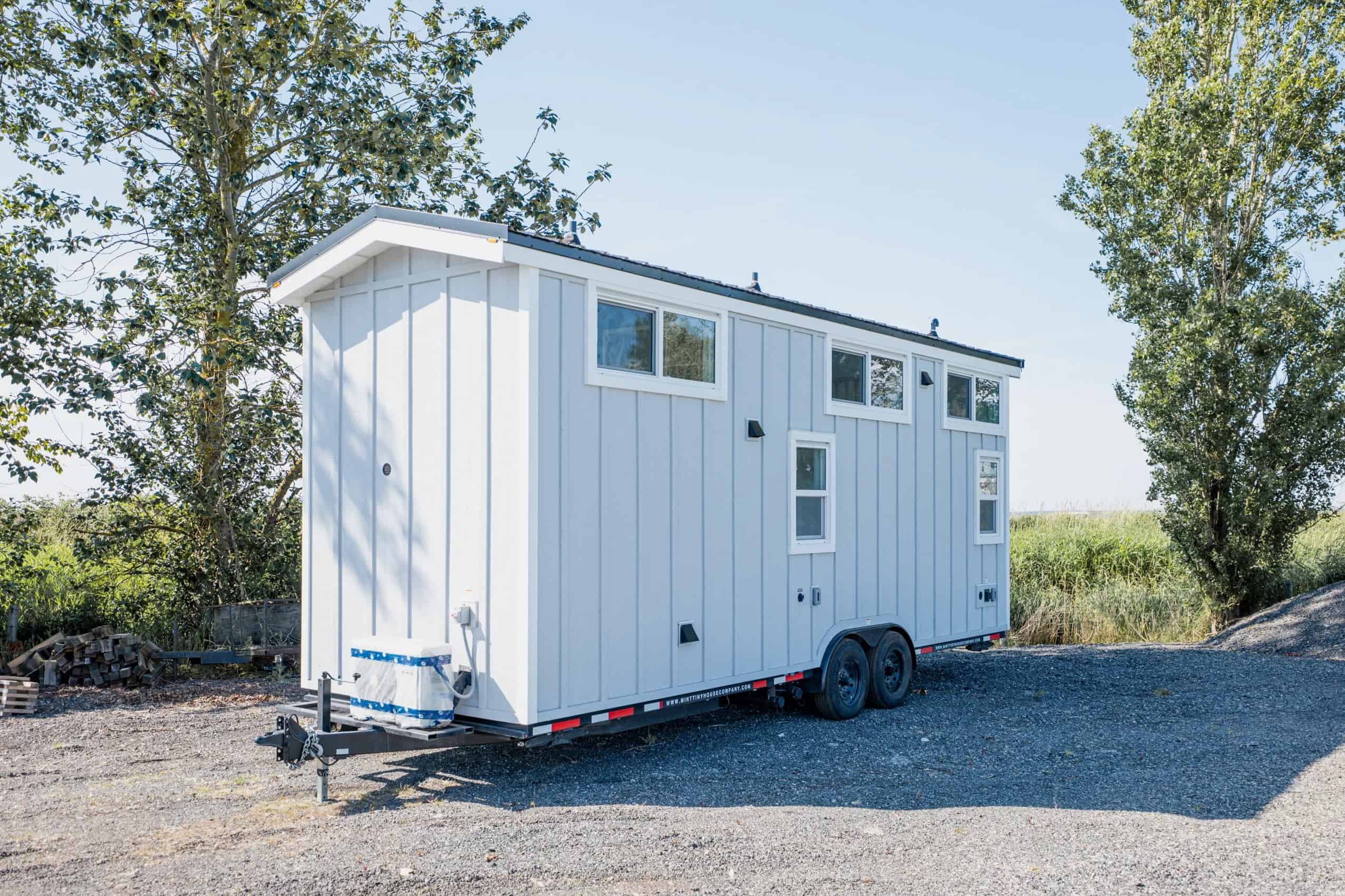 Mint STR 26 tiny house on a dual-axle bumper-pull trailer: light grey vertical siding, white trim, dark standing-seam roof, high loft windows, white mini-split on the tongue