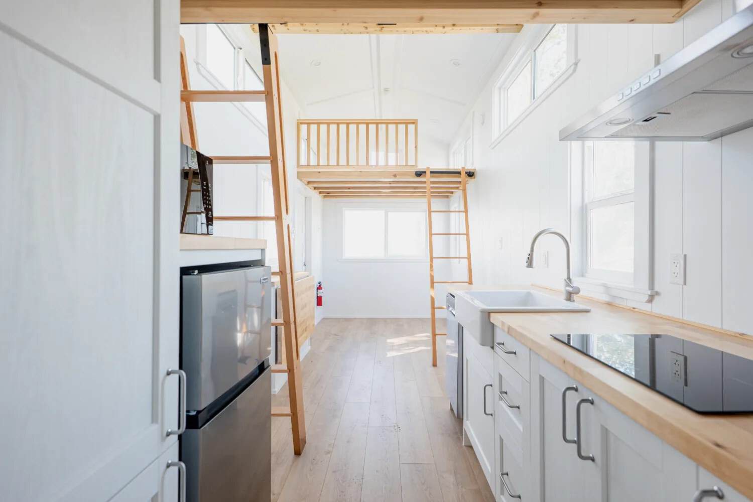 Galley of the STR 26: white cabinets, butcher-block veneer, apron sink, two-burner cooktop, stainless fridge, two wood ladders to the sleeping lofts