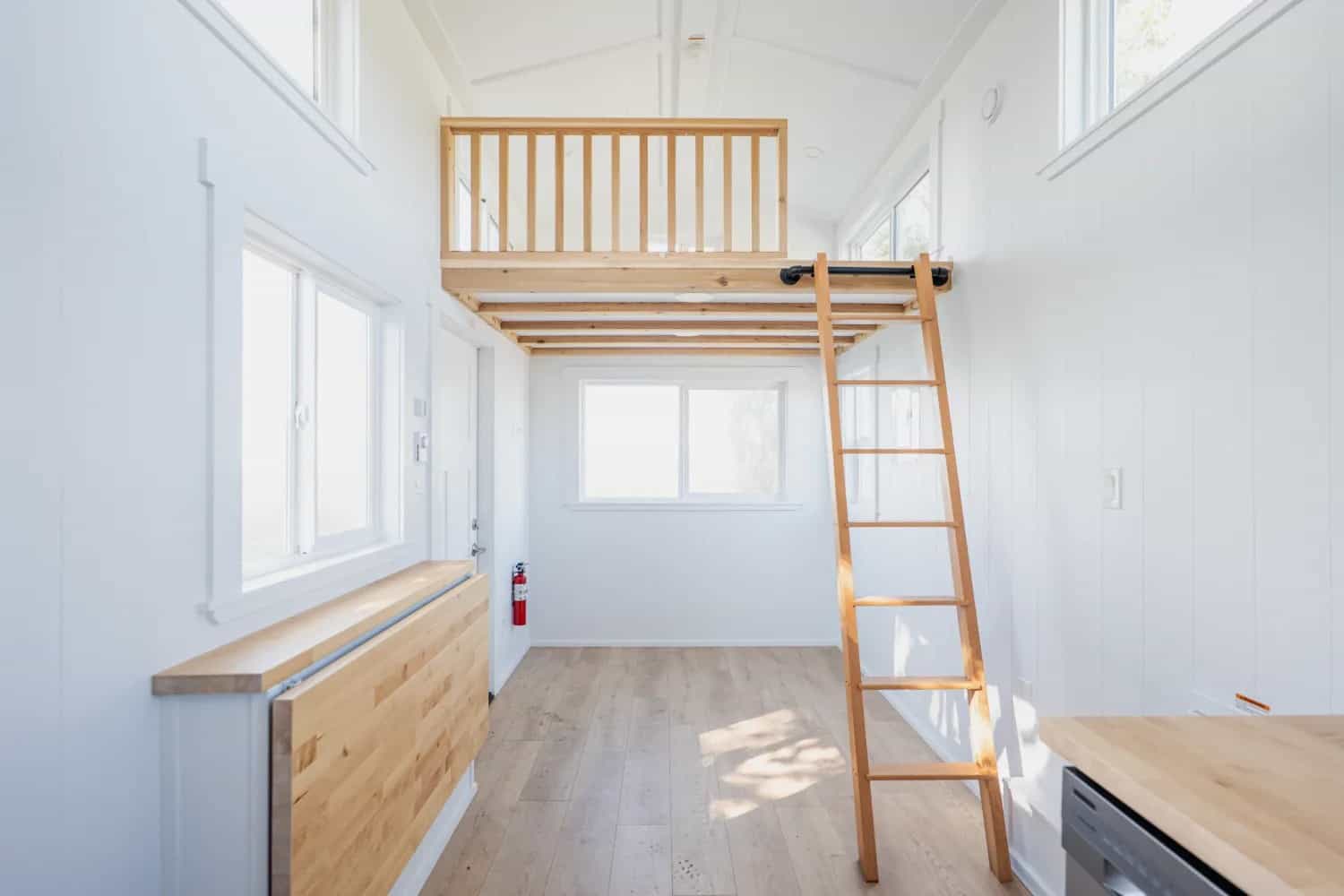 Bright white interior of the STR 26: fold-down butcher-block table under a window, wood loft ladder, loft railing, light plank floor toward the galley