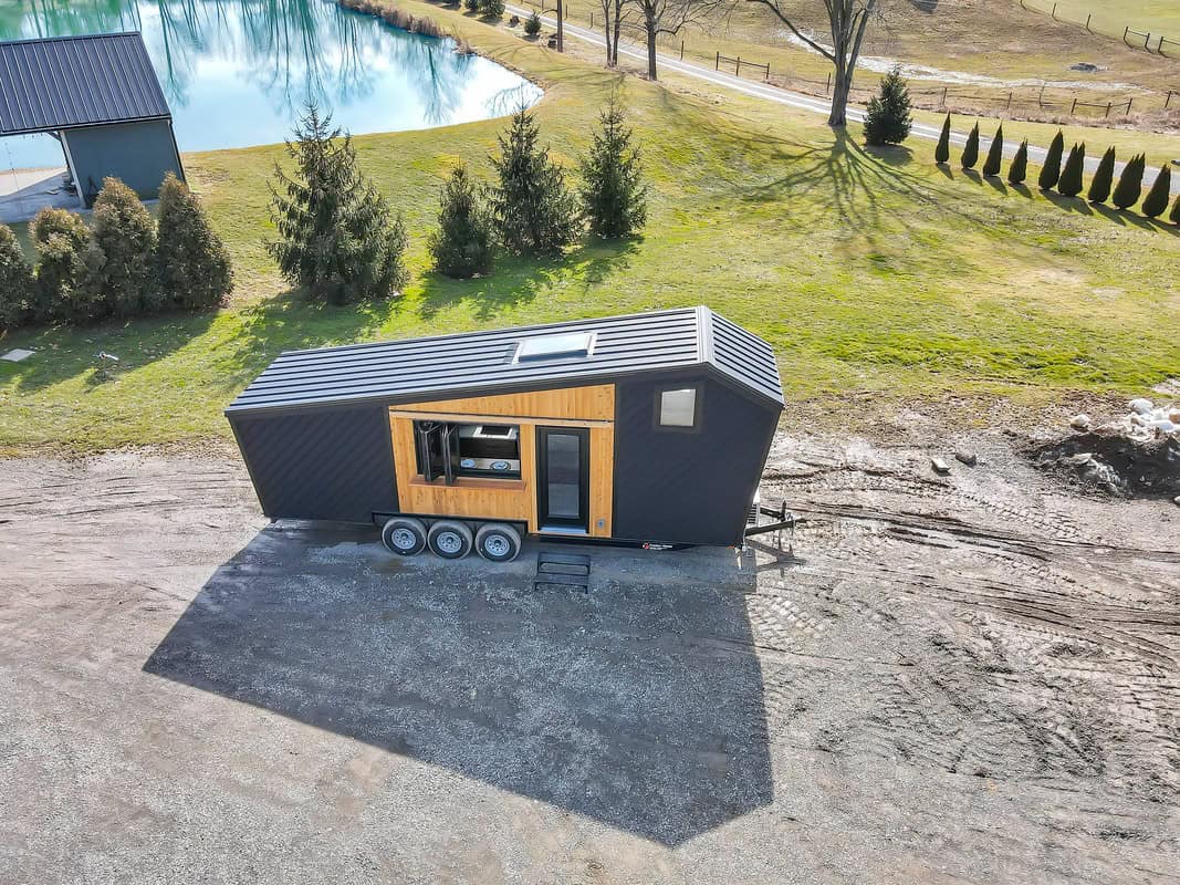Aerial view of Modern Tiny Living Catalina: black steel roof, black LP siding with cedar accent, flip-up bar window, dual-axle trailer
