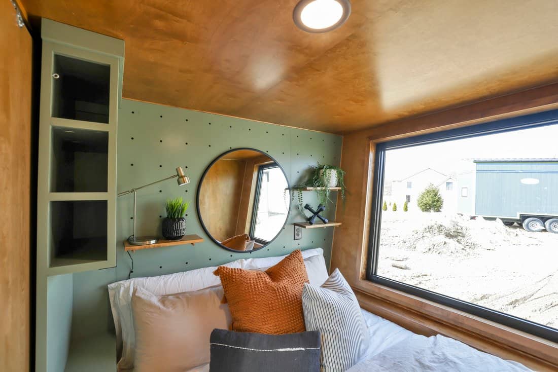 First-floor bedroom in the Modern Tiny Living Catalina with a sage pegboard wall, round mirror, built-in shelves and a large picture window