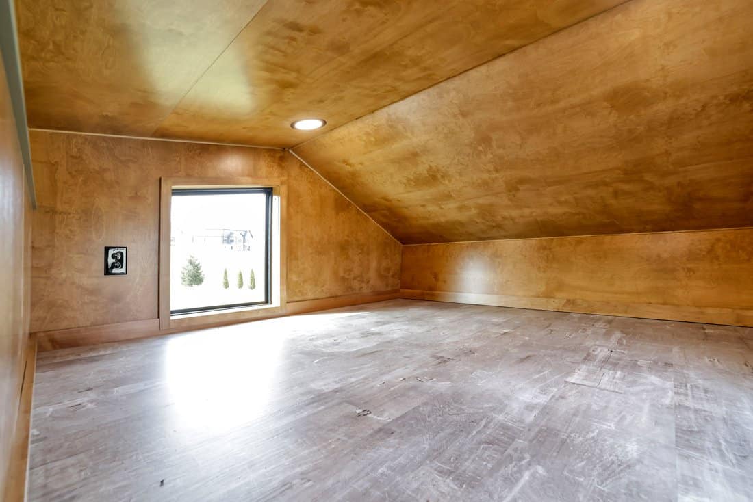 Empty king-size loft in the Modern Tiny Living Catalina with sloped maple ceiling, small square window and recessed light