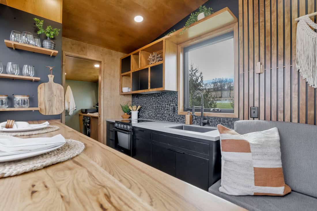 Modern Tiny Living Catalina kitchen: stained maple plywood, open shelving, large sink, LVP floor under the saltbox volume