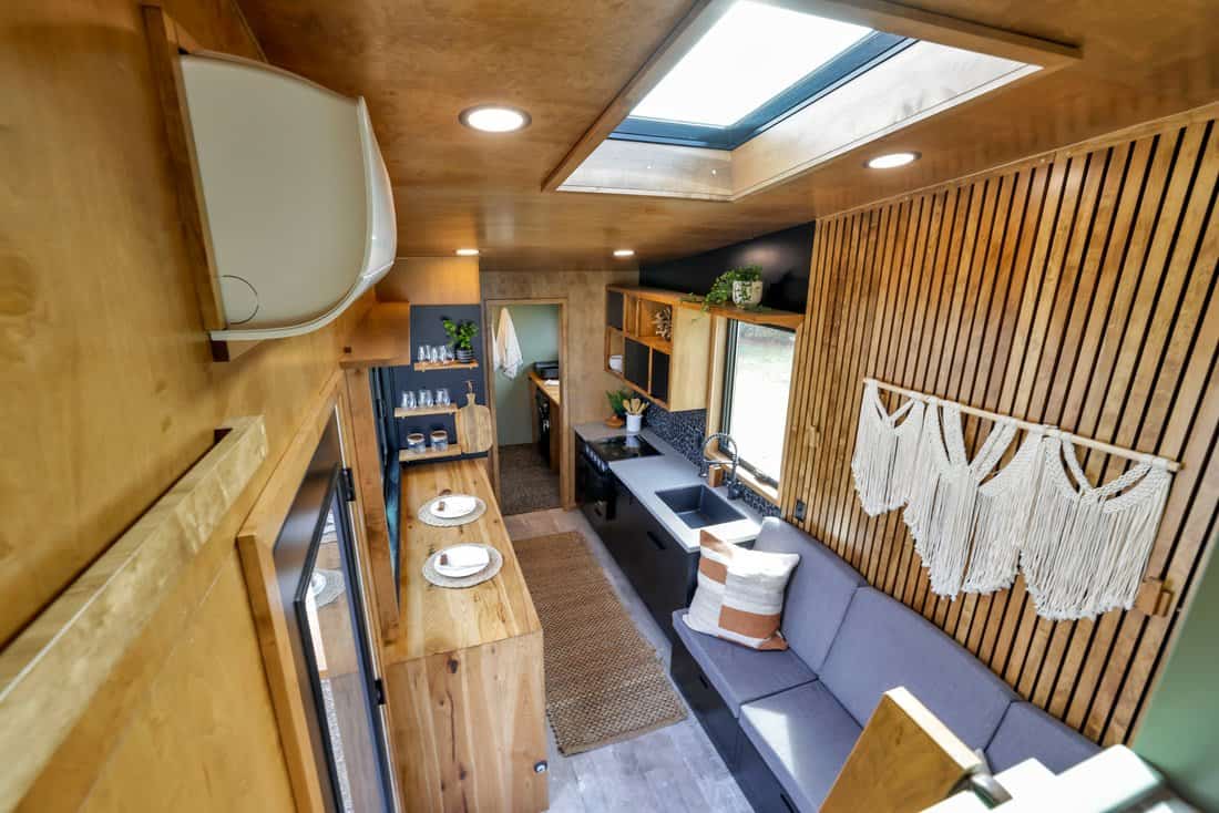 Looking down the Modern Tiny Living Catalina: skylight, mini-split, bar counter, kitchen, gray sofa and slatted wood wall with macrame