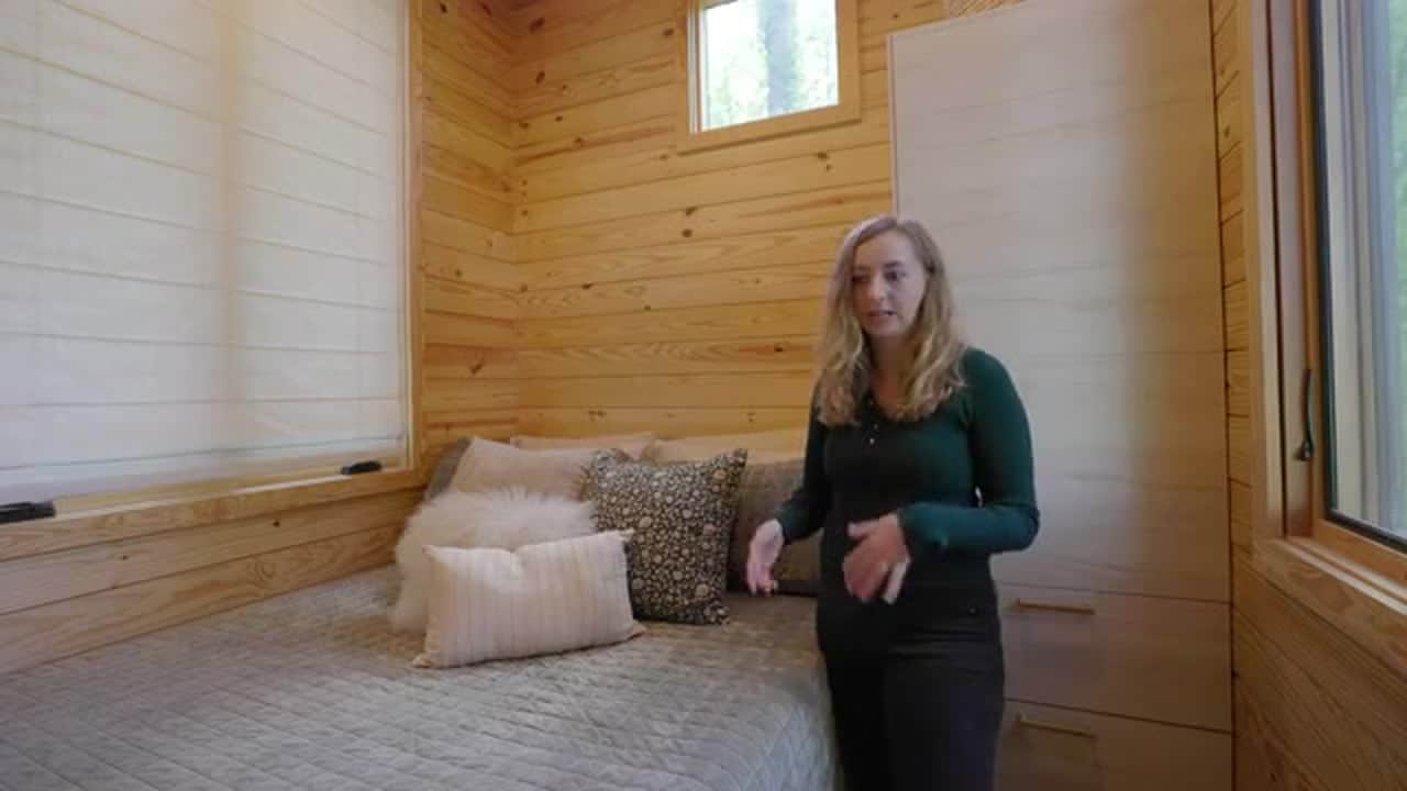 Ground-floor bedroom of the no-loft cottage: grey quilt, floral pillow, wood-plank walls, built-in wardrobe