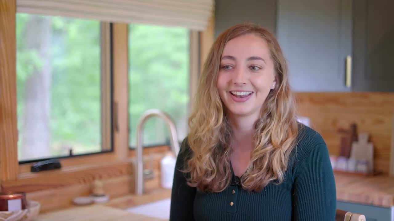 Mollie in the kitchen of her no-loft cottage, gooseneck faucet and wood-framed window behind her
