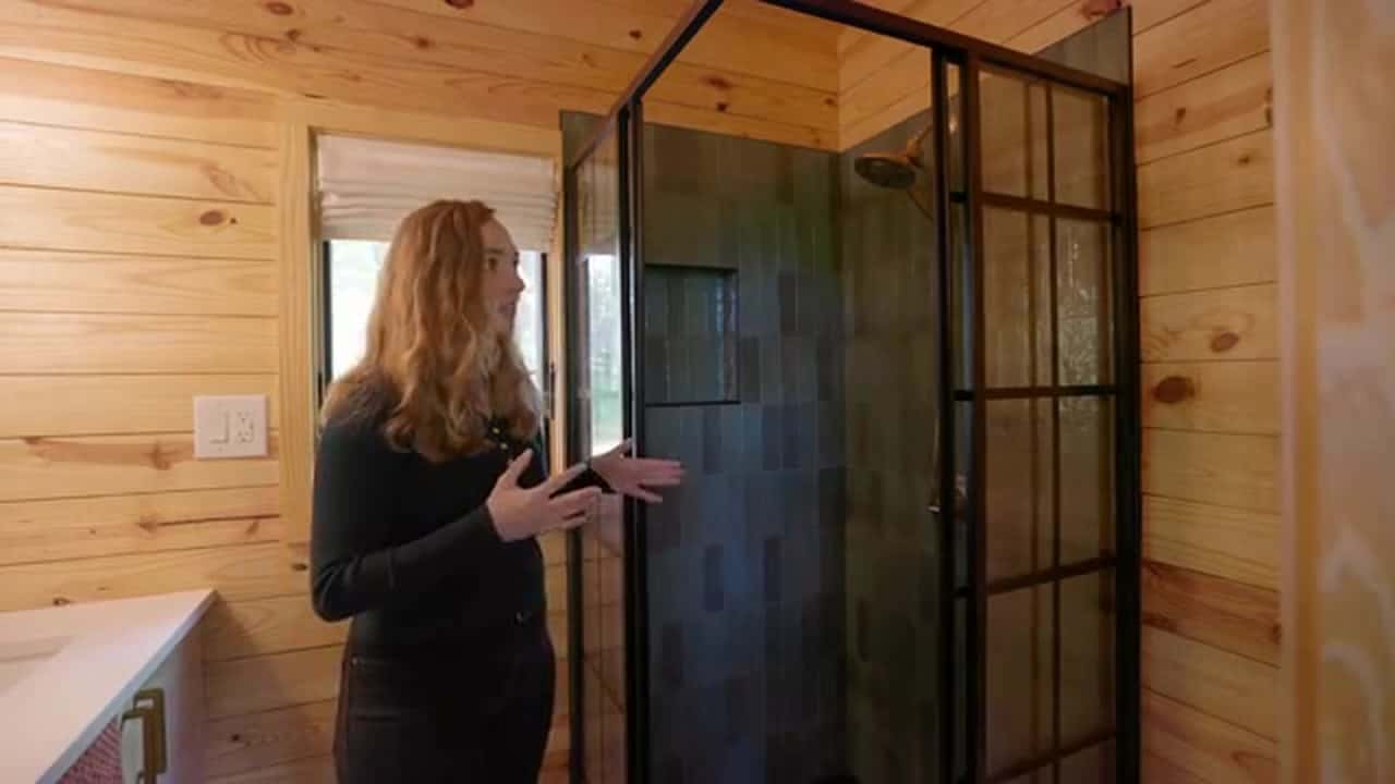 Bathroom shower with black-framed glass, dark green tile, and a gold showerhead, wood-plank walls