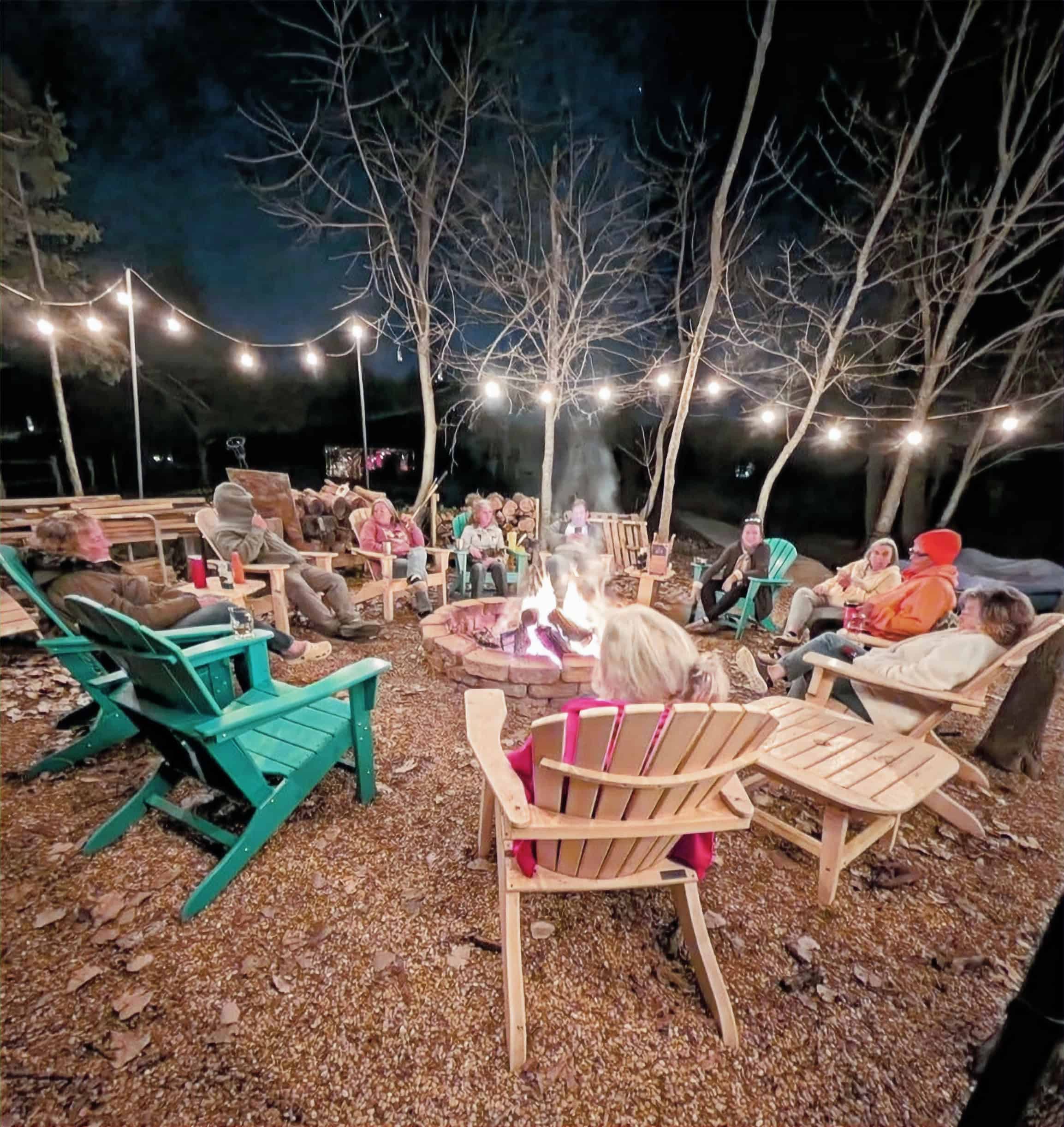 Night gathering around a stone fire pit, Adirondack chairs, and string lights at Monarch Springs Ranch in Celeste, Texas