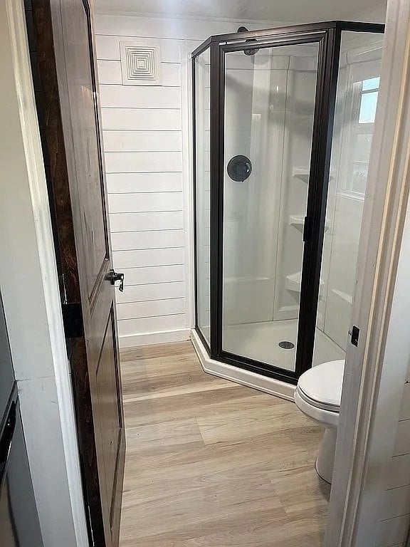 Bathroom of the Mustard Seed Sprout with a neo-angle glass shower, white toilet, shiplap walls, and wood-look flooring