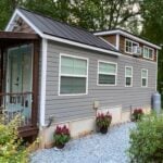 Mustard Seed Sprout tiny house with grey siding, cedar-shingle loft, aqua French doors, and a wooden porch on a wooded lot at Lakewalk in Greer, South Carolina
