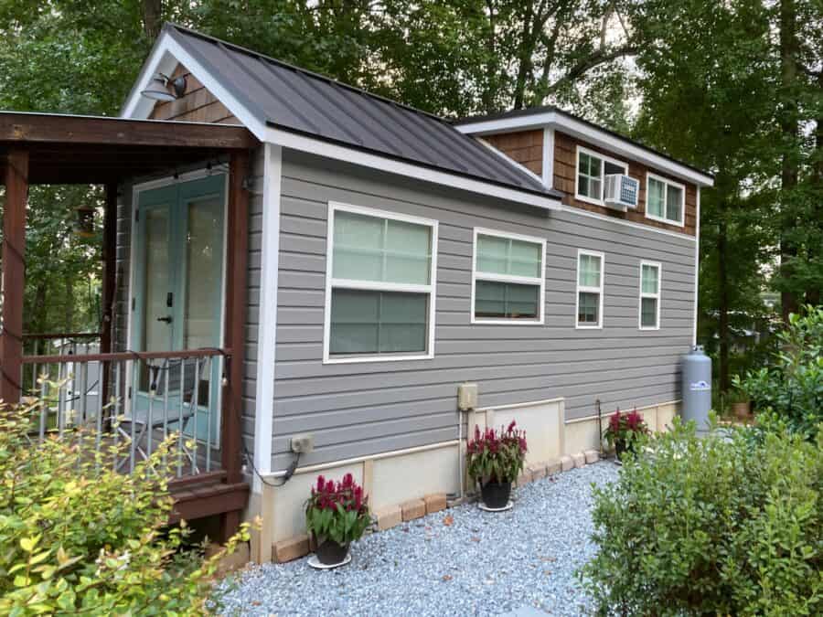 Mustard Seed Sprout tiny house with grey siding, cedar-shingle loft, aqua French doors, and a wooden porch on a wooded lot at Lakewalk in Greer, South Carolina