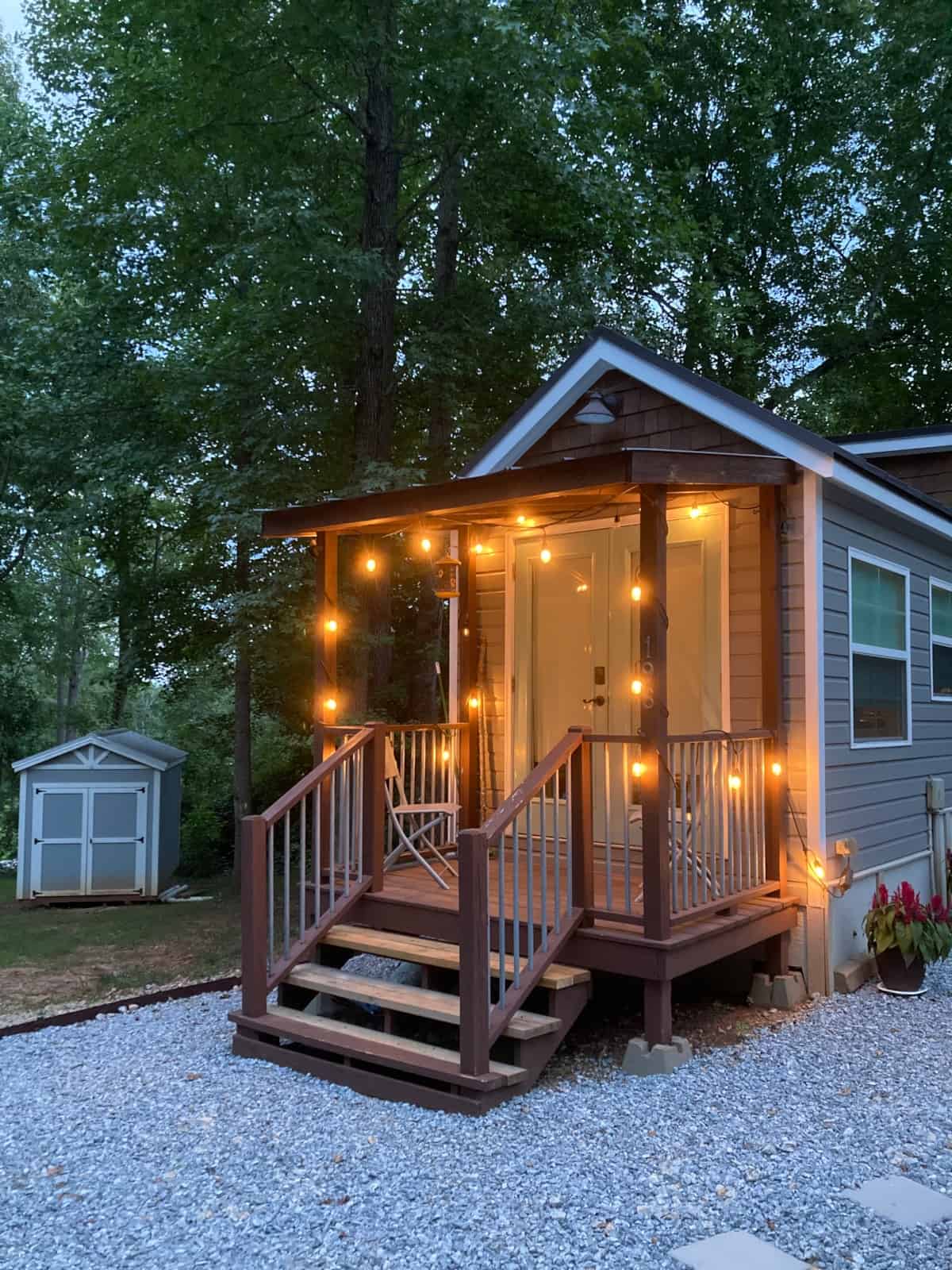 Dusk view of the Mustard Seed Sprout porch and grey siding with string lights; 8x10 shed visible in the background