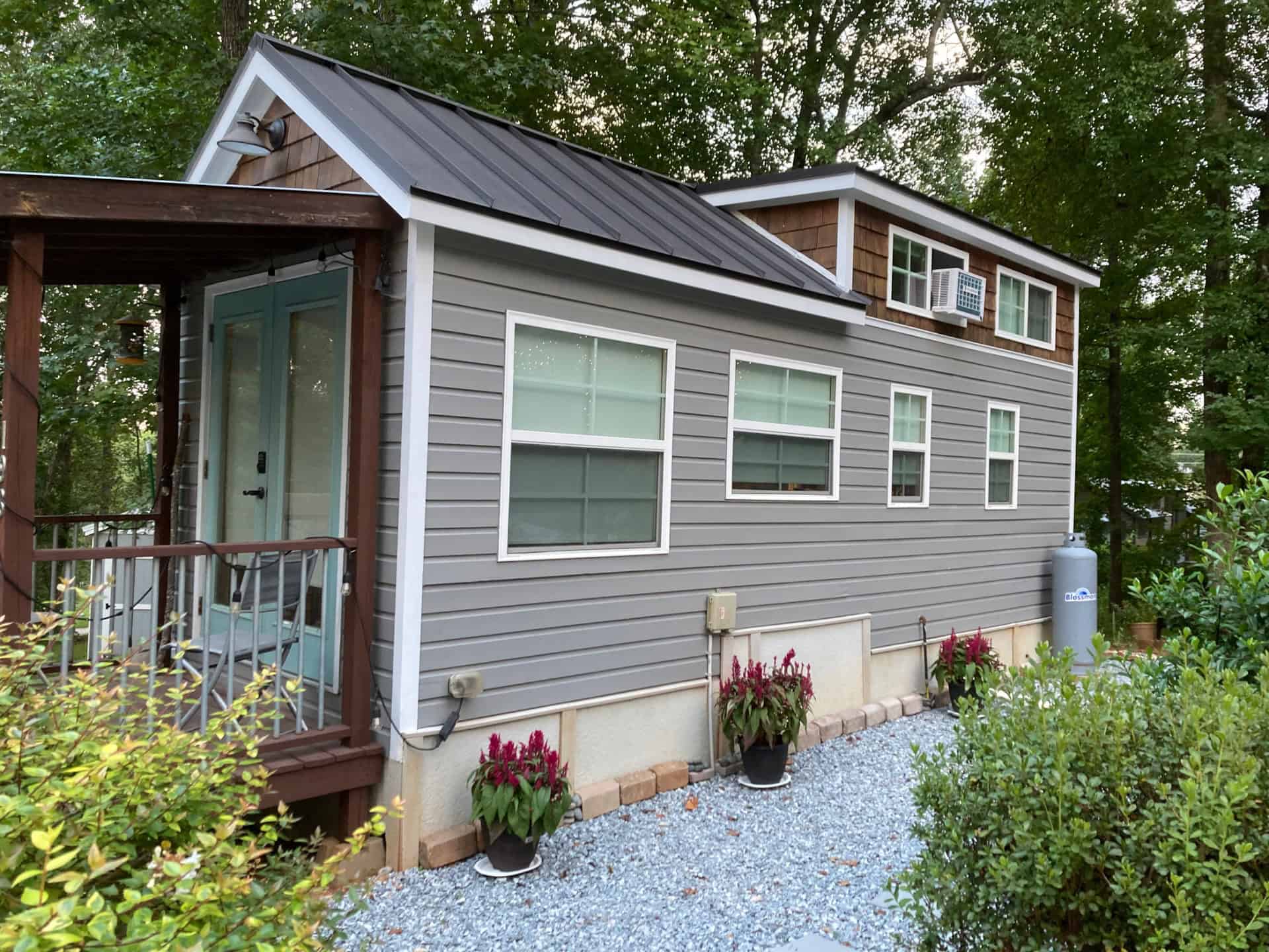 Mustard Seed Sprout tiny house with grey siding, cedar-shingle loft, aqua French doors, and a wooden porch on a wooded lot at Lakewalk in Greer, South Carolina