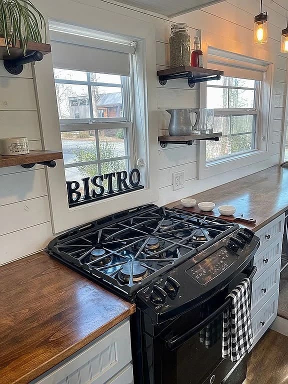 Kitchen of the Mustard Seed Sprout with a full-size black gas range, butcher-block counters, open pipe shelves, and white shiplap walls
