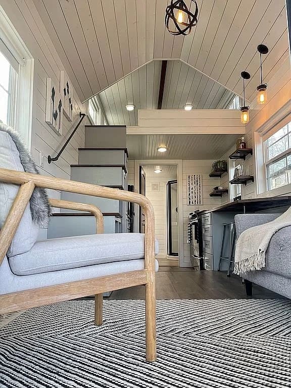 Living area of the Mustard Seed Sprout looking toward the kitchen, storage stairs, and sleeping loft, with white shiplap and a vaulted ceiling