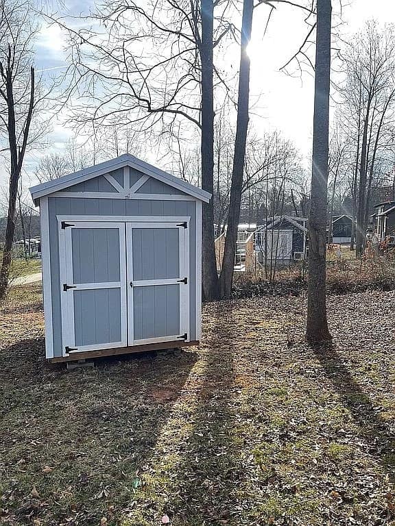 Detached 8x10 shed with blue-grey siding, white trim, and double doors on the wooded lot at Lakewalk Tiny Home Community
