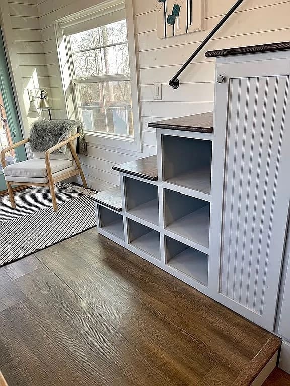 Storage stairs with dark wood treads, cubbies, and a black pipe handrail beside a large living-area window