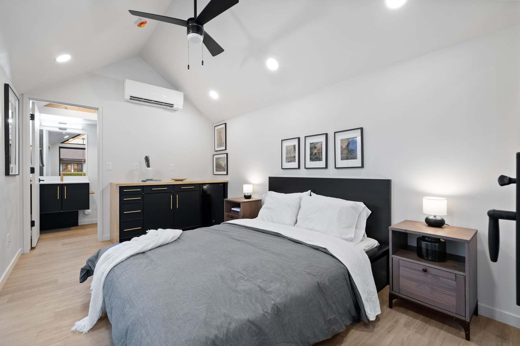 ADU bedroom with a vaulted ceiling, ceiling fan, wall-mounted mini-split, and a vanity visible through the doorway