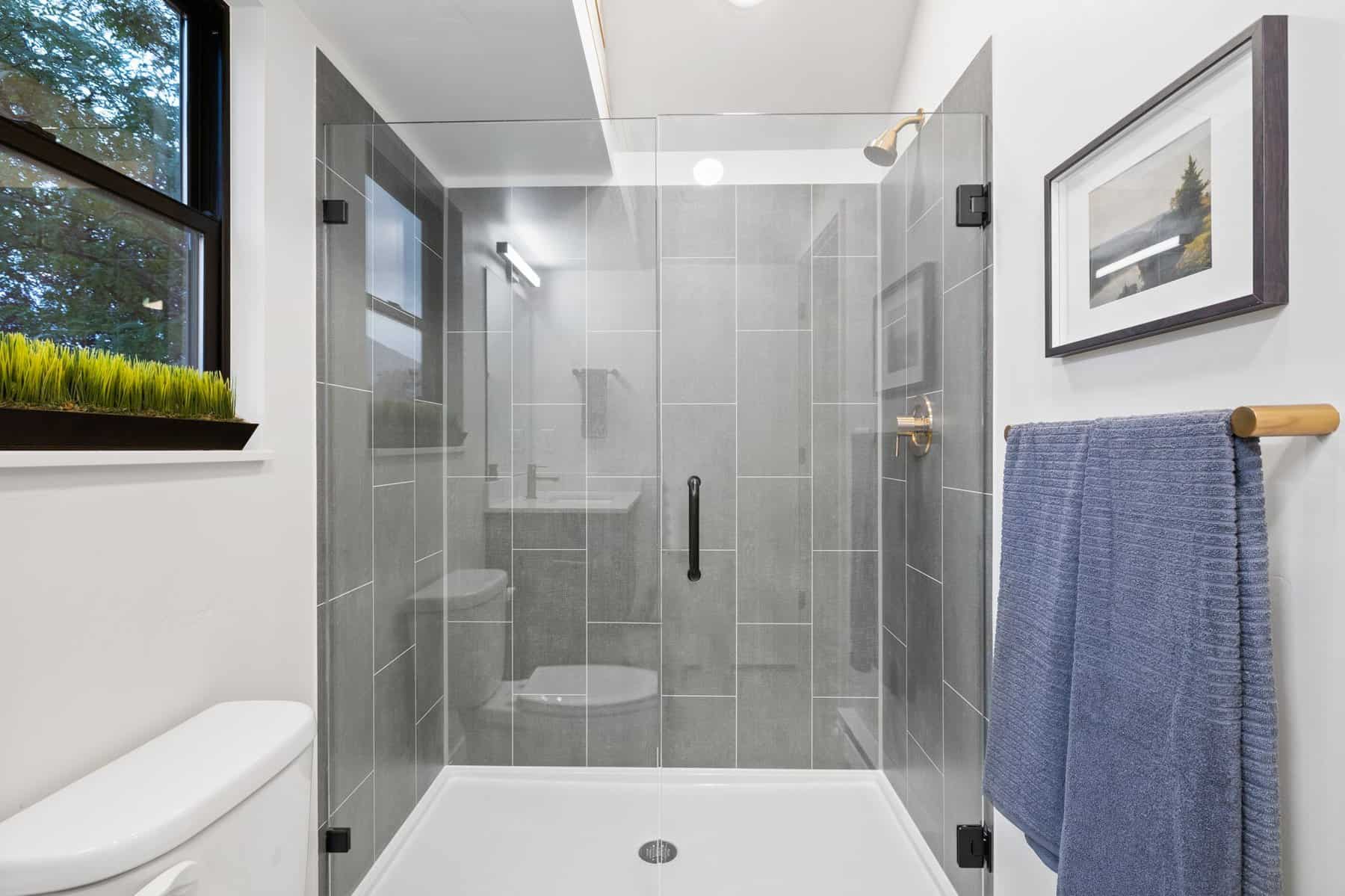 ADU bathroom with a glass-enclosed tiled shower, a window, and a blue towel on a wall bar
