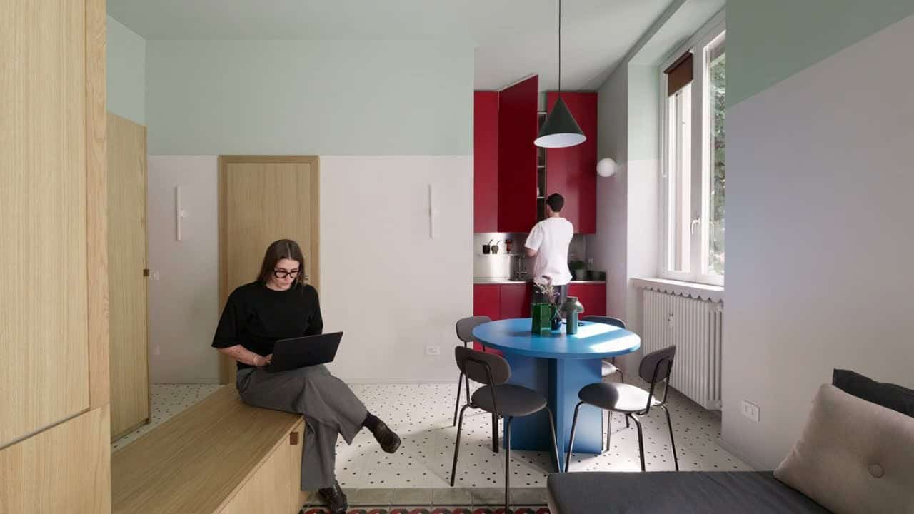 Open living dining kitchen with blue round table, deep-red kitchen recess, sage upper walls, and terrazzo-inspired floor
