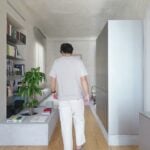 Man walking away down Casa VA’s living run: granite platform with a circular planter and books, recessed wall shelves, freestanding grey storage unit, stainless kitchen counter at the right edge