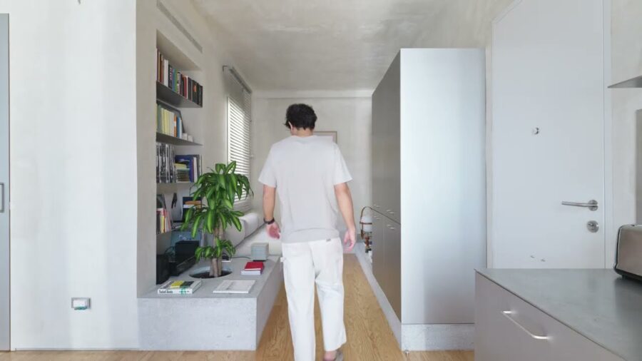 Man walking away down Casa VA’s living run: granite platform with a circular planter and books, recessed wall shelves, freestanding grey storage unit, stainless kitchen counter at the right edge