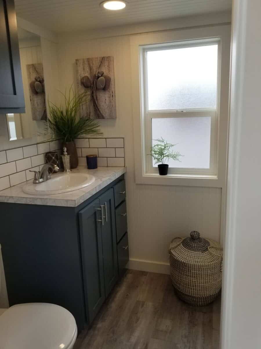 Bathroom with a blue-gray vanity and sink, subway tile, a medicine cabinet, a frosted window, and a toilet