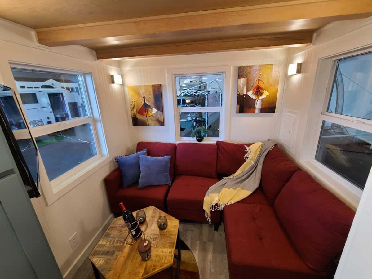 Main-floor room with a red sectional sofa, wood coffee table, three windows, and wood beams overhead