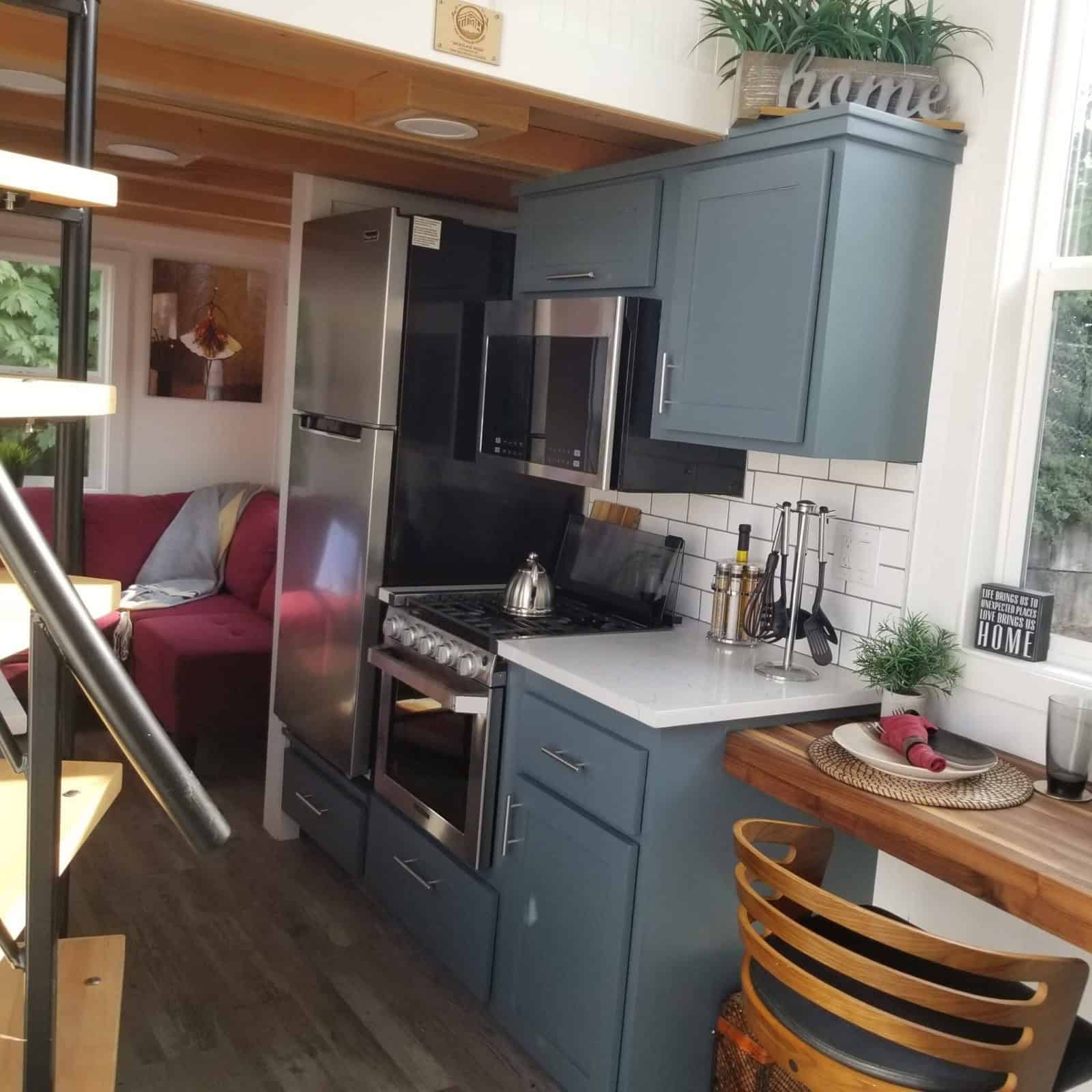 Galley kitchen with blue-gray shaker cabinets, a stainless refrigerator, a stainless range and over-the-range microwave, white counters, and subway tile
