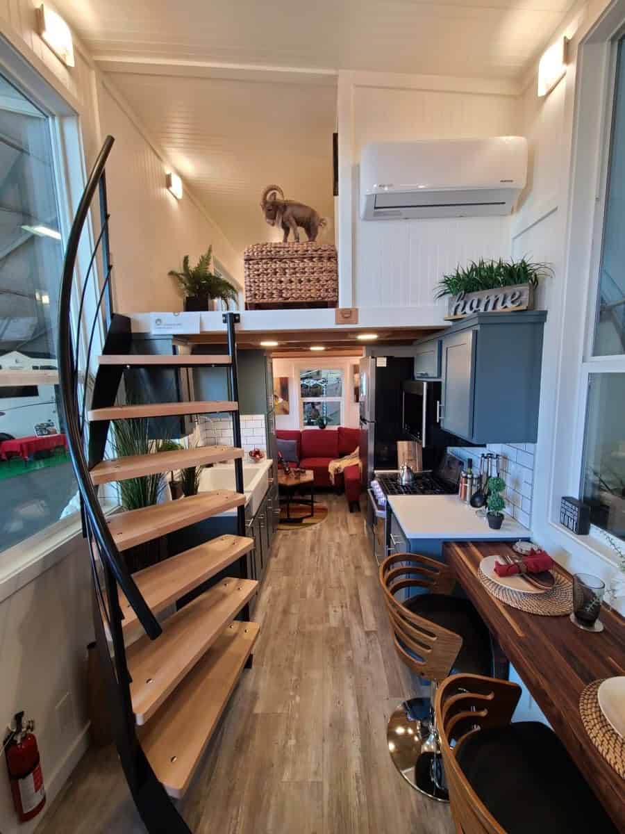 Long interior view past a curved open staircase and a wood snack bar with stools, through the galley kitchen to a red sectional in the flex room