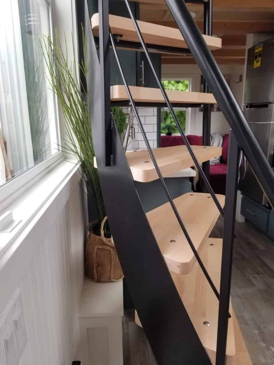 Black steel staircase with light wood treads beside a tall window