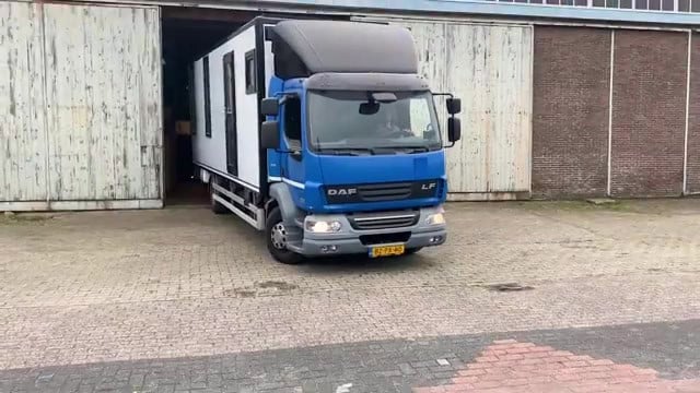 Blue DAF LF cab and white living box pulling out of a warehouse onto brick paving