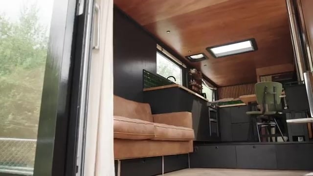 Full-length cabin view: sofa, kitchen run, raised desk platform, skylights, wood stove flue