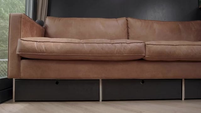 Tan leather sofa with three black under-seat drawers on herringbone wood floor