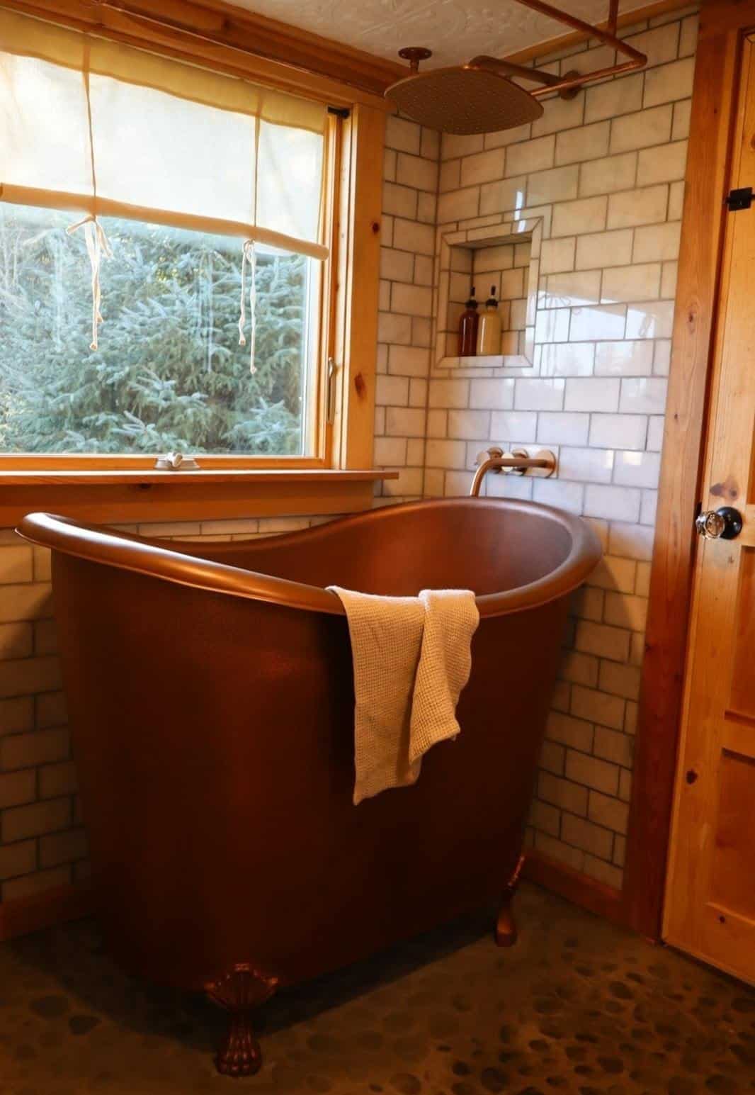 Solid hammered copper clawfoot tub on a river rock floor in the tiny house bathroom