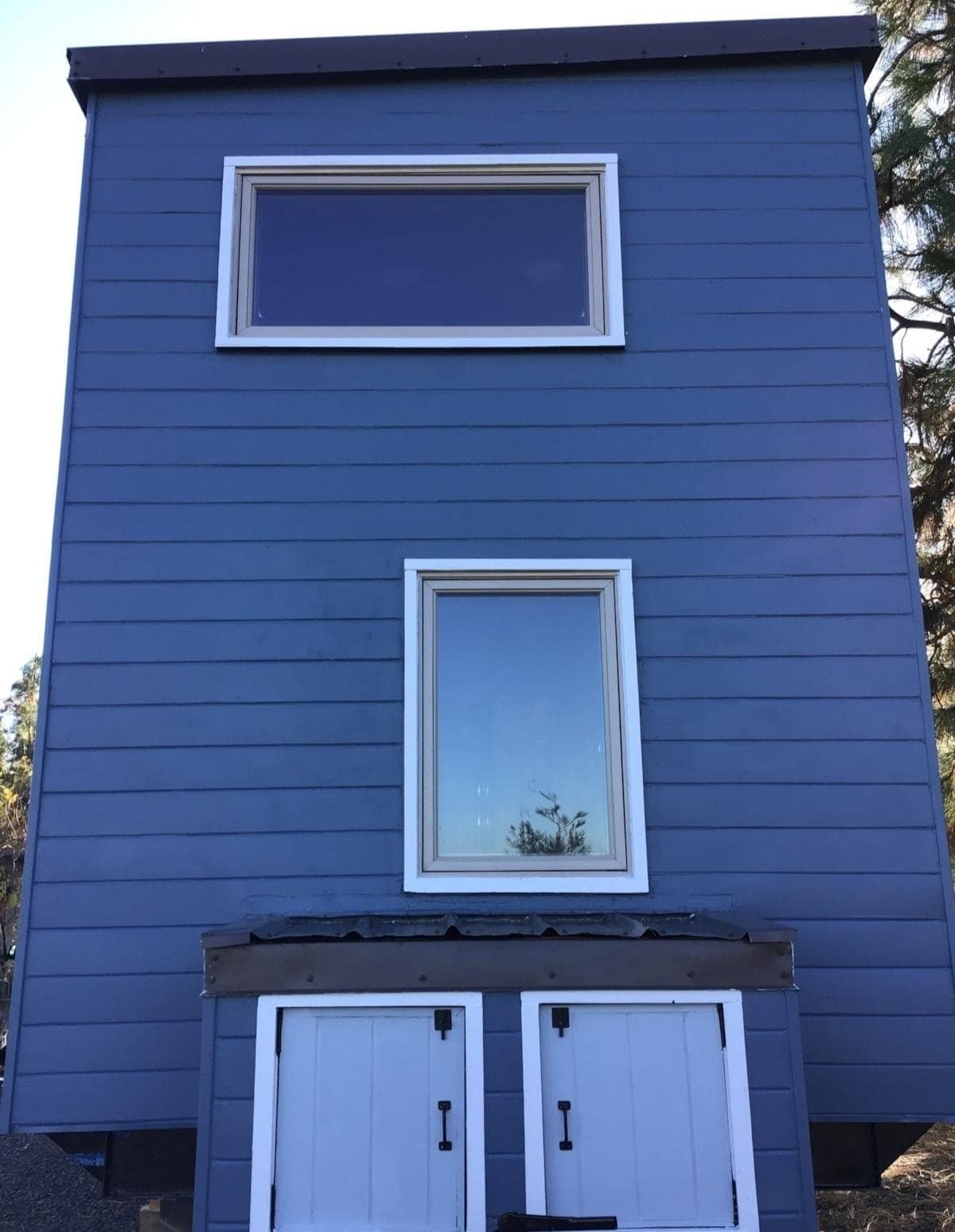 Gable end of the navy blue tiny house showing loft windows and lower doors
