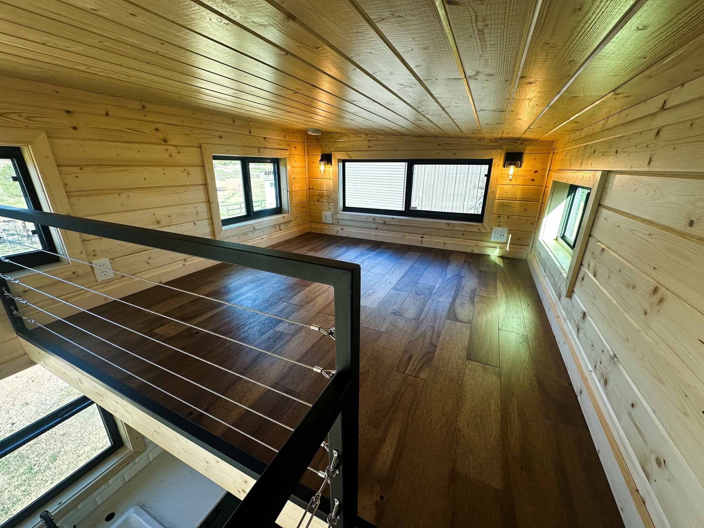 Nomad sleeping loft: light wood tongue-and-groove, dark floor, black cable rail, black-framed windows, industrial wall sconces