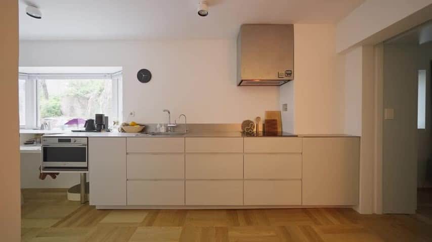 Kitchen wall with white drawers, an oven, a steel hood, and a window