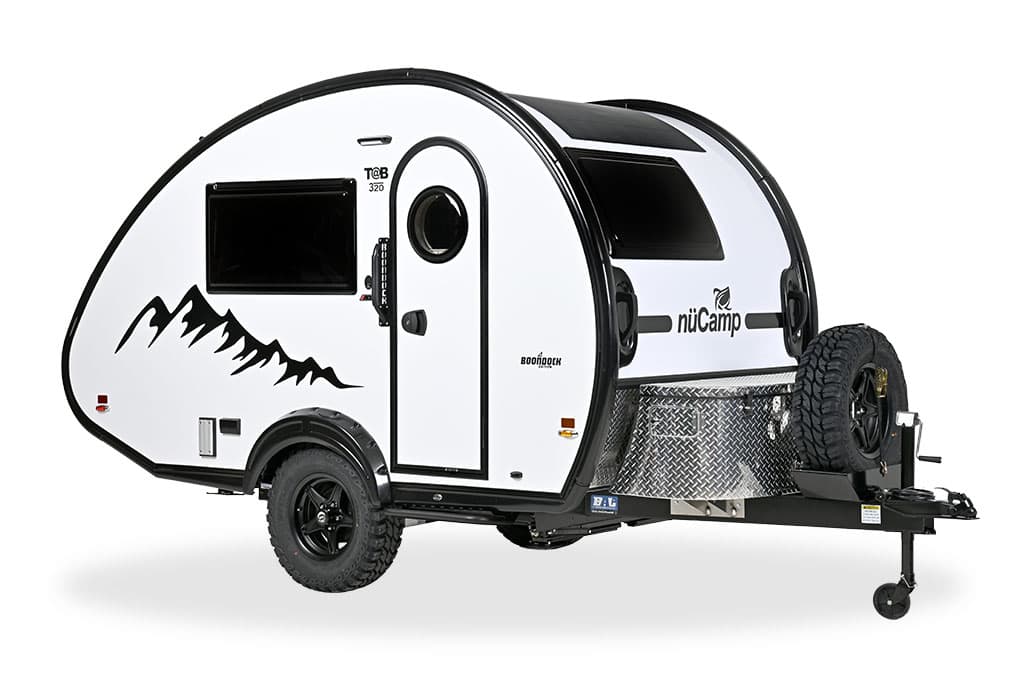 White 2026 nuCamp TAB 320 Boondock Edition teardrop, three-quarter studio: porthole door, mountain graphic, diamond-plate tongue box, spare tire