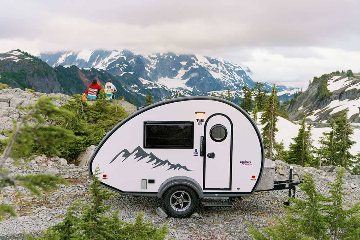 White 2026 nuCamp TAB 320 Boondock Black Canyon teardrop parked on a rocky mountain overlook, side profile, snow peaks behind