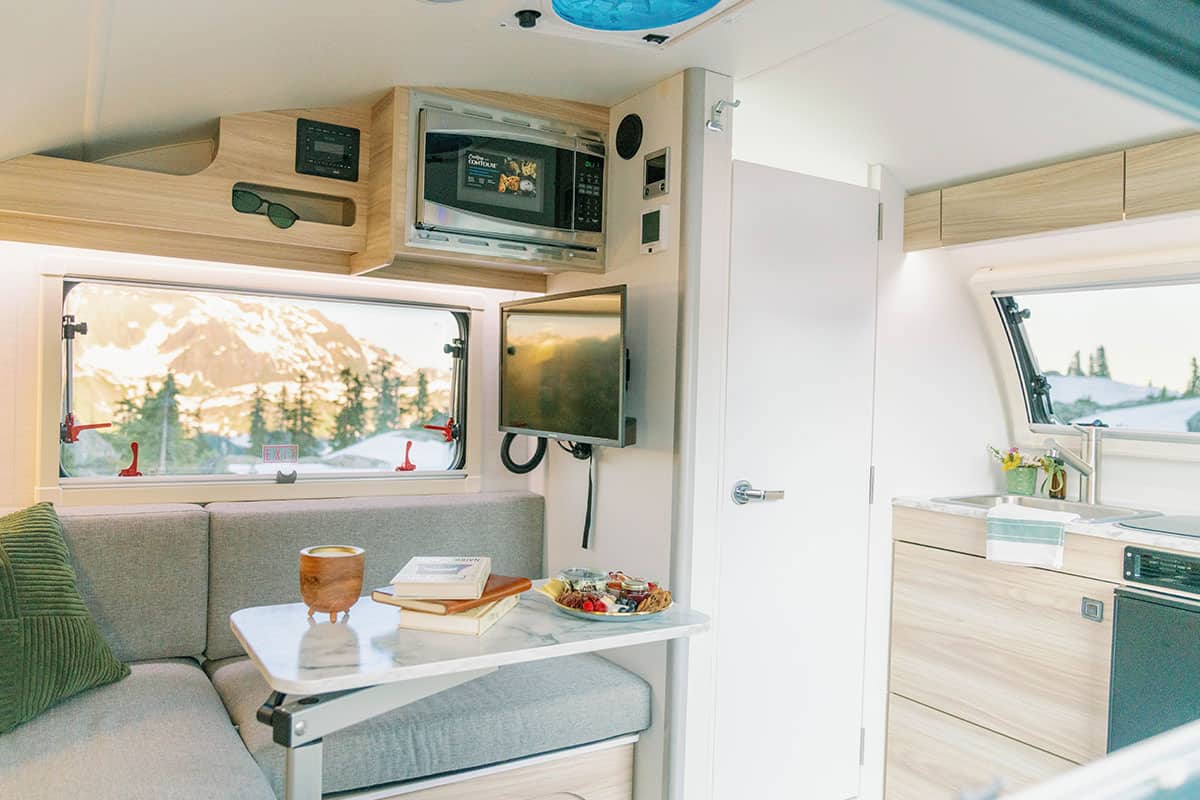 Interior of the 2026 nuCamp TAB 320: grey dinette, marble-look table, stainless sink, 12-volt fridge, and a white bath door