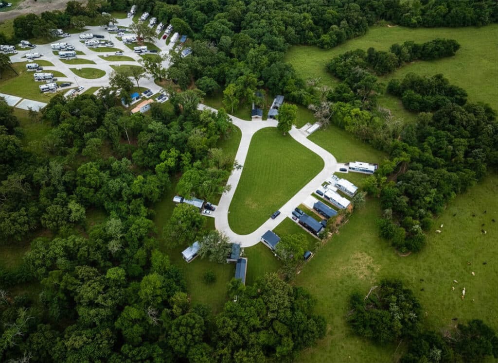 Aerial view of a concrete loop with tiny-home pads around a central lawn at The Oaks on 37 in Mount Vernon, Texas