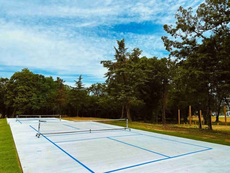 Two outdoor pickleball courts with blue lines and portable nets beside trees at The Oaks on 37 in Mount Vernon, Texas