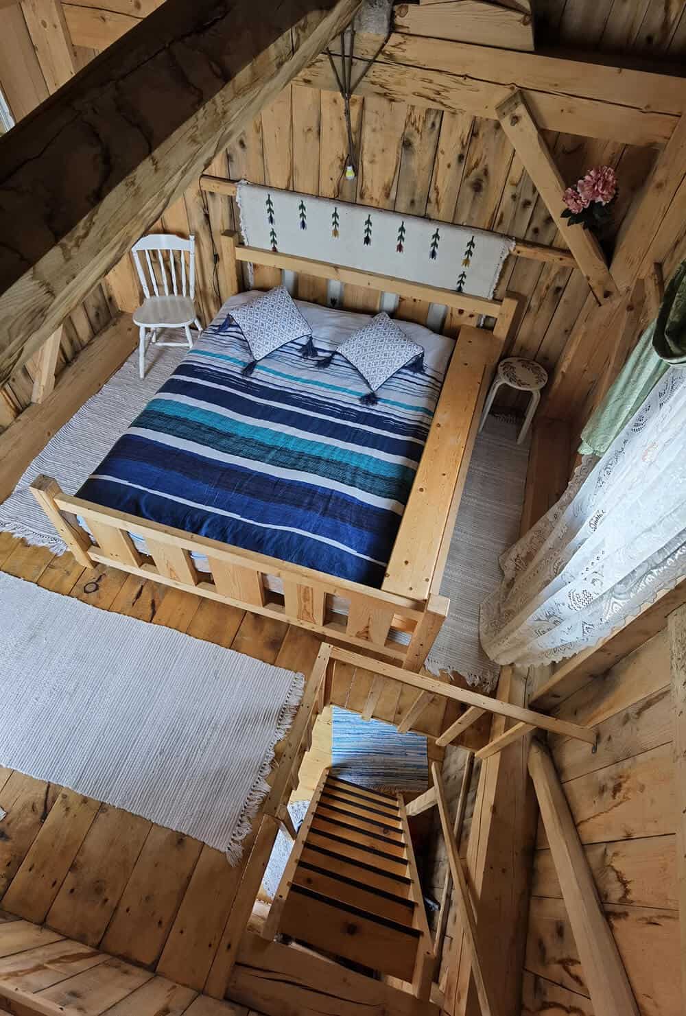 Upstairs loft of Ohessaare Tuulik: large double bed with blue striped duvet, steep wood stairs