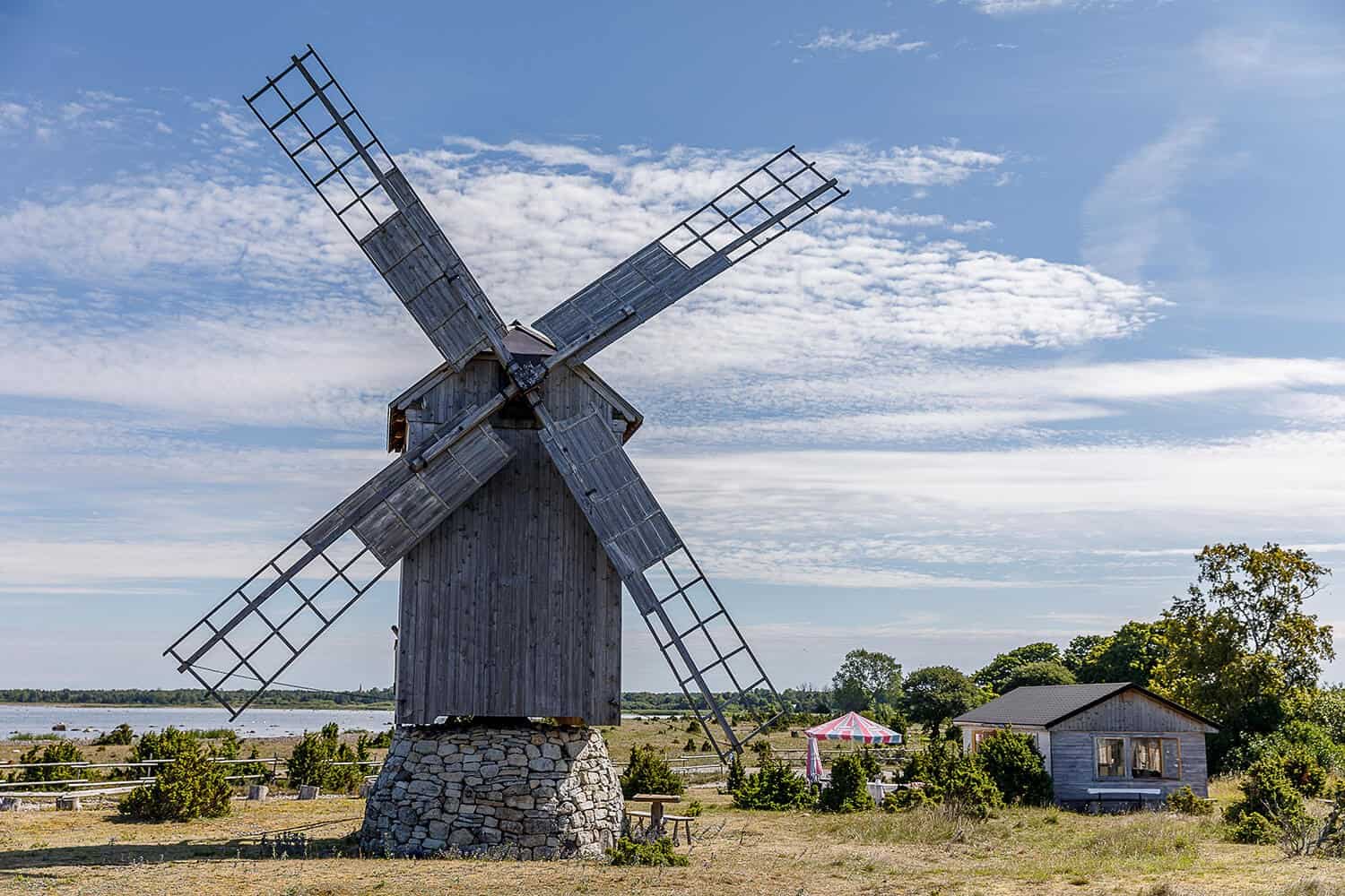 Ohessaare Tuulik exterior: picnic table, small wooden outbuilding, sea behind the mill