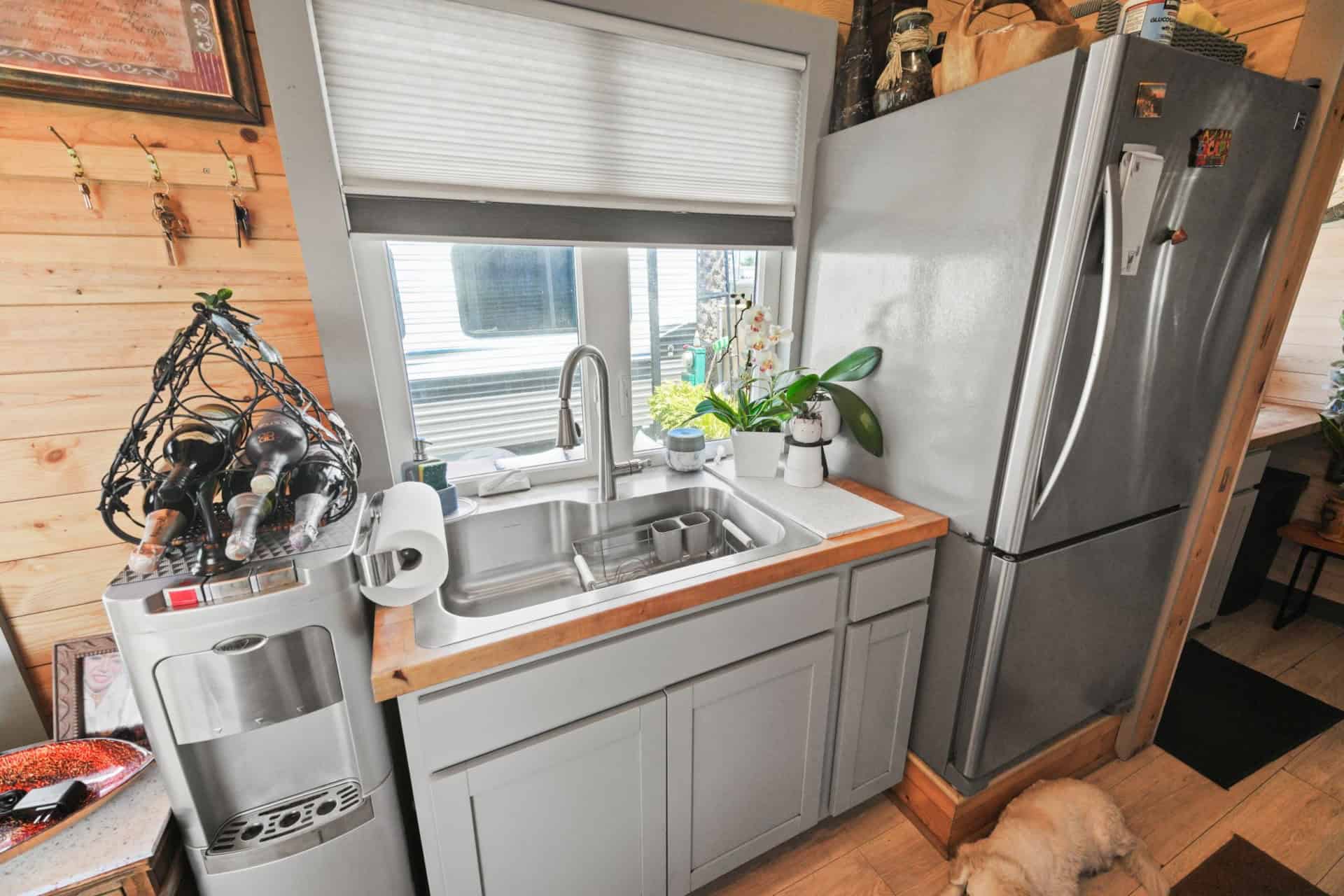Tiny house kitchen with a deep sink under a window, butcher block counters and a full-size stainless refrigerator