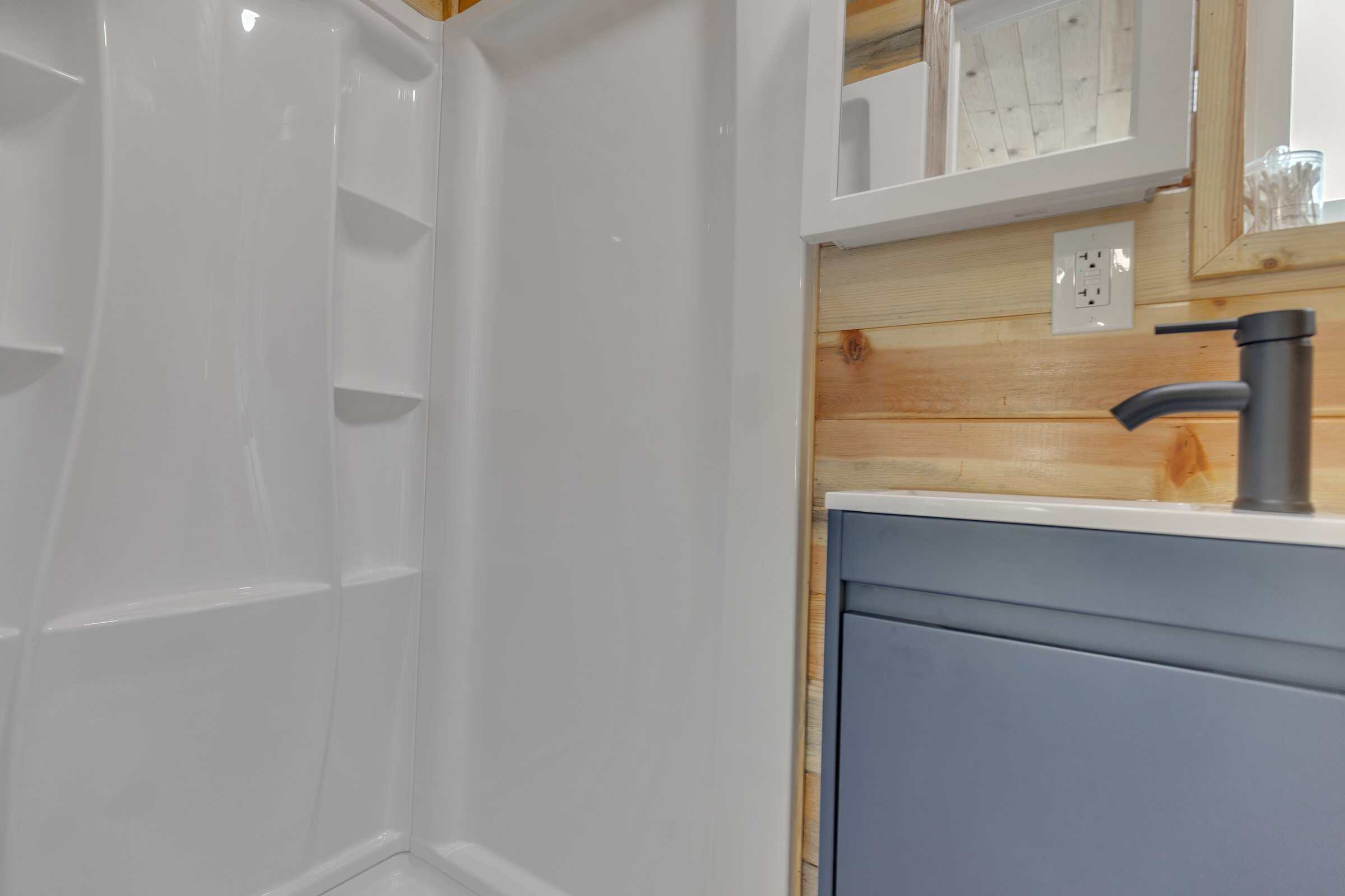 Pacifica Model X bathroom: white 36-inch shower stall with recessed shelves, navy vanity, white sink, black faucet, wood walls